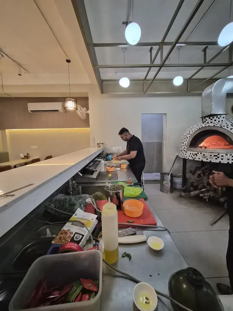 A pizzaiolo working at the mosaic oven behind the counter